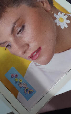 Woman wearing a crocheted daisy earring with white petals and a yellow center.