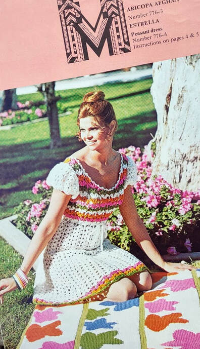 Estrella peasant dress. Woman with a crocheted dress with a colorful top, white puff sleeves and a white skirt. Sitting on a flower afghan with flowers around an oak tree in the background