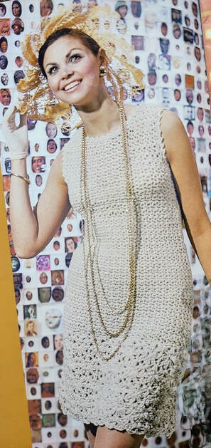 Woman with a fancy gold hair piece wearing a Cream colored sleeveless crocheted dress and a long gold necklace