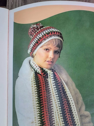 Woman with bangs wearing a beret with cream, brown, red and green stripes.
